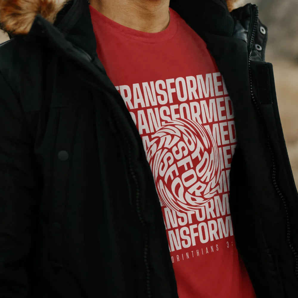 A man in a field wearing a red 'Transformed' Christian T-shirt from 3rd Day's Christian clothing collection.